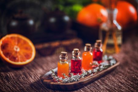 Bottles filled with red and orange essential oils on wooden board. Fresh citrus fruit, orange and lime cut in half. Aromatherapy relax conceptの写真素材