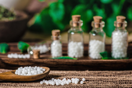 Wooden spoon and small bottles full of homeopathic globules, mint leaves in backgroundの写真素材