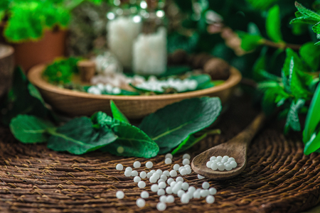 Wooden spoon full of homeopathic globules, small bottles with homeopathic pills and mint leaves in backgroundの写真素材