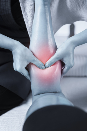 Close up image of physiotherapist massaging female patient with injured leg. Blue colored image. Red accent on the calf muscle painの写真素材