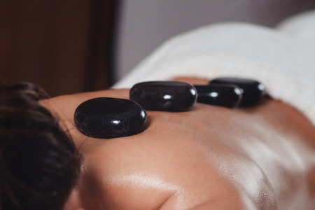 Young woman getting hot stone massage at spa salon, lying on massage tableの写真素材