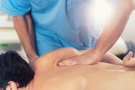 Physiotherapist doing healing treatment on man's back. Therapist wearing blue uniform. Osteopathy. Chiropractic adjustment, patient lying on massage tableの写真素材