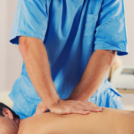 Physiotherapist doing healing treatment on man's back. Therapist wearing blue uniform. Osteopathy. Chiropractic adjustment, patient lying on massage tableの写真素材