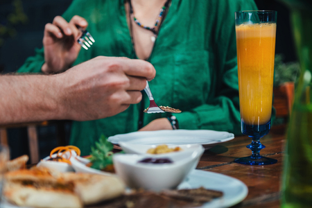 Couple enjoying romantic vegetarian dinner, drinking fresh orange juice on a date. Couple sitting at wooden table, wearing colorful outfit.の写真素材