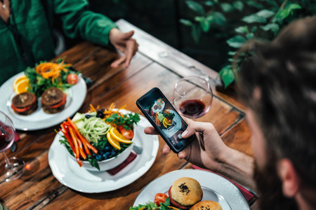Cropped shot of young couple photographing delicious vegetarian burger and mixed organic salad on white plate in vegetarian restaurant.の写真素材