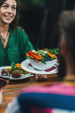 Vertical image of waiter serving plate of delicious vegetarian mixed organic salad in restaurant to...