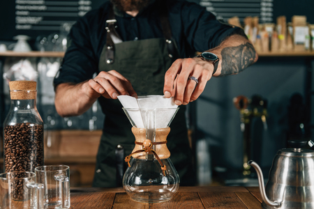 Close up image of barista hands preparing filter for coffee. Barista with tattooed arms wearing dark uniform.の写真素材