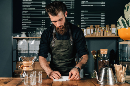 Young male barista preparing filter for coffee. Barista with tattooed arms wearing dark uniform.の写真素材