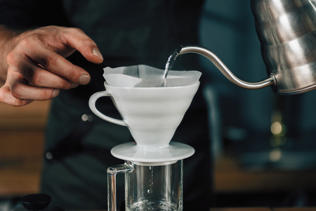 Male barista hands pouring boiling water from kettle to Drip coffee maker.の写真素材