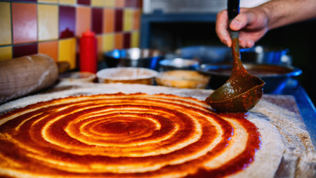 Chef spreading tomato sauce on pizza dough with a metal ladle in pizza restaurant. Pizza Making Process.の写真素材