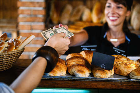 Beautiful smiling female bakery assistant dressed in black uniform selling croissant.