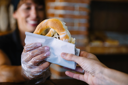 Female bakery worker gives salty pretzel to customer.の写真素材