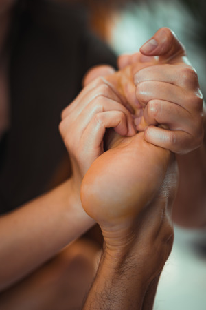 Physiotherapist massaging male patient with injured foot muscle. Sports injury treatment.の写真素材