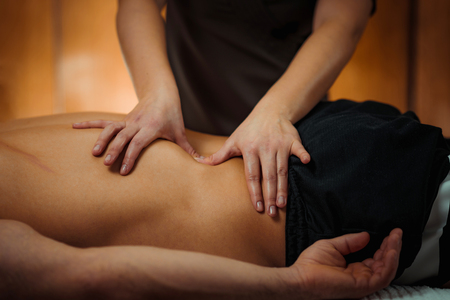 Physiotherapist massaging male patient with injured lower back muscle. Sports injury treatment.