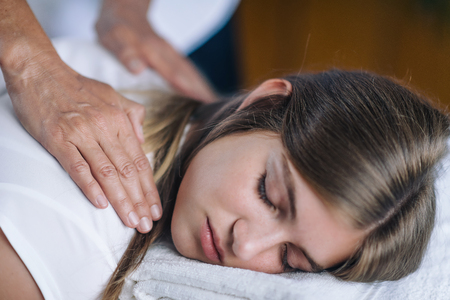 Vertical image of female Reiki therapist holding hands over shoulders of the patient and transfer energy. Peaceful teenage girl lying with her eyes closed. Alternative therapy concept of stress reduction and relaxation.の写真素材