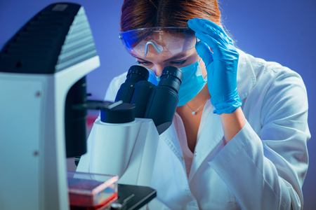 Biology researcher looking through microscopeの写真素材
