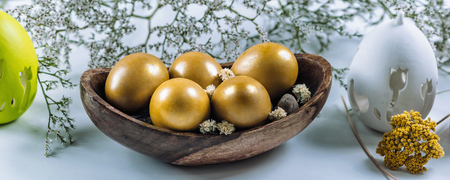 Close up image of golden Easter eggs in wooden bowl.  Green grass and dried flower decor. Easter...