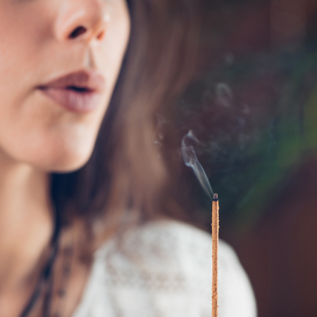 Beautiful Caucasian girl blowing smoke from burned incense stick.の写真素材