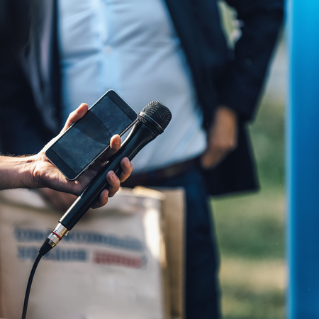 Press conference event. Male hand holding mobile phone and microphone. Recording sound at outdoor...
