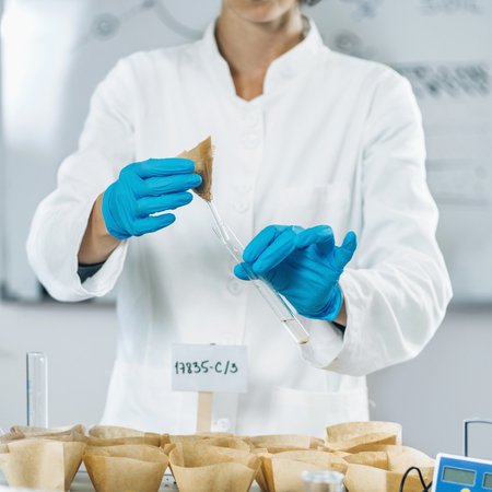 Soil Samples Testing Laboratory. Woman biologist in white coat pouring water in soil sample.
