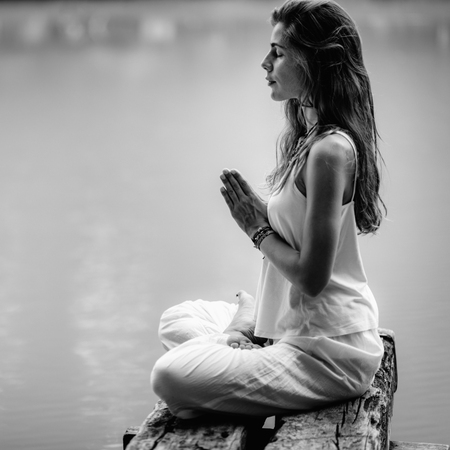 Young woman meditates, practicing yoga in nature. Sitting in lotus pose with hands in prayer position.の写真素材
