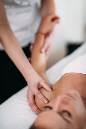 Physiotherapist massaging female patient with injured shoulder.  Sports injury treatment.の写真素材