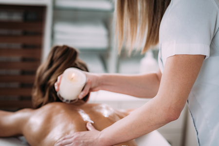 Physiotherapist drips wax from candle and massaging female patientâs back.の写真素材