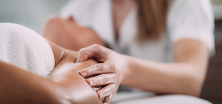 Physiotherapist massaging female patient with injured shoulder.  Sports injury treatment.の写真素材