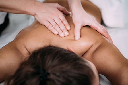 Physiotherapist massaging female patient with injured shoulder blade.  Sports injury treatment.の写真素材