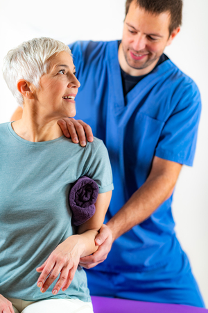 Therapist Checking Senior Womanâs Arm in Physical Therapy Officeの写真素材
