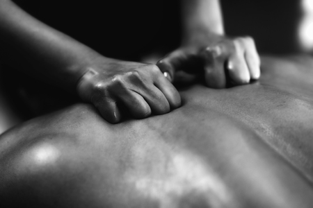 Physiotherapist massaging male patient with injured back muscle. Sports injury treatment.の写真素材