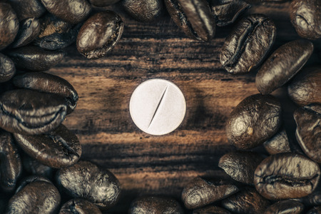 White caffeine pill surrounded by roasted coffee beans on wooden backgroundの写真素材