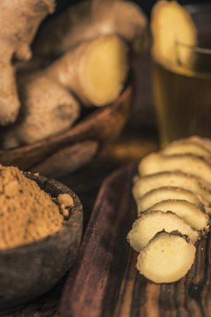Sliced ginger root and ginger powder in the bowl on the table. Anti-inflammatory herbal medicine