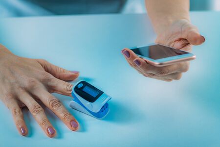 Woman Using Pulse Oximeter and Smart Phone, Measuring Oxygen Saturationの写真素材