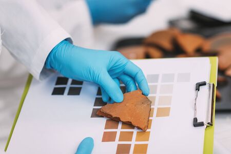 Young archaeologist compare pottery color with color chart scheme in laboratory.の写真素材