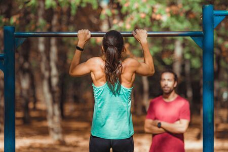 Woman doing pull-ups in the park with personal trainerの写真素材