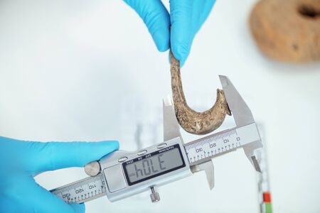 Young archaeologist measuring ancient hook with digital caliper.の写真素材