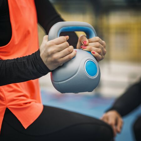 Young sporty woman lifting kettlebell, working with personal fitness trainer.