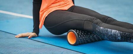 Close up image of attractive female athlete, stretching with foam roller, outdoorsの写真素材