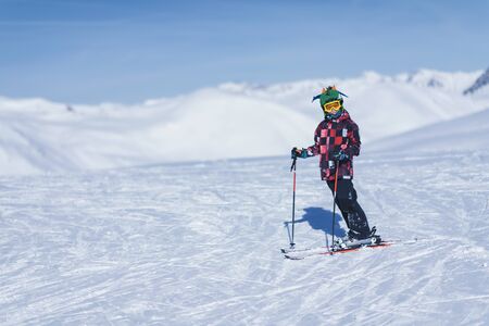 Young male skier in colorful outfit on top of mountain ski resort. Copy space for text.