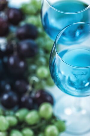 Two wine glasses with blue wine and grapes in the backgroundの写真素材