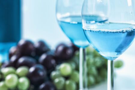 Two wine glasses with blue wine and grapes in the background