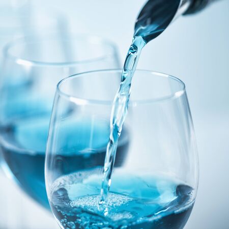 Pouring blue wine with splash and bubbles into a wine glass, close up