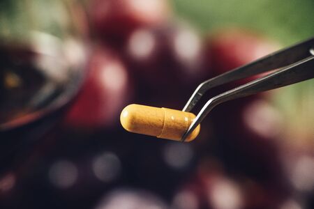 Resveratrol supplements with blurred grapes and glass of red wine in background. Macro shot, focus...
