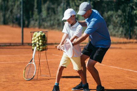 Boy Training with Tennis Instructor on a Clay Courtの写真素材