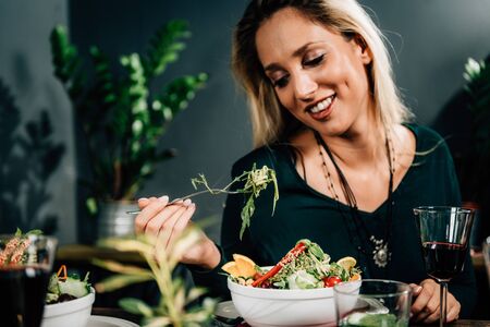 Vegetarian Restaurant. Cheerful Female Friends Enjoying Fresh Salad in Restaurant and Having Fun.の写真素材