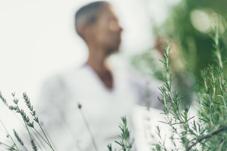 Dreamy Mindful Middle Aged Woman Expressing Positivity, Dressed in White, Enjoying the Scent of Rosemary.の写真素材