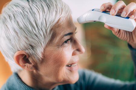Smiling Senior Woman Measuring Body Temperature with Non-Contact Digital Thermometer