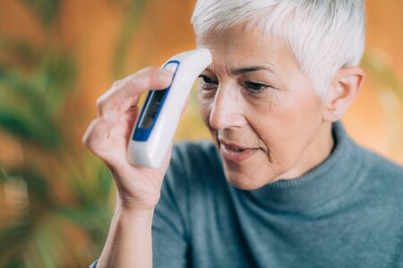 Senior Woman Measuring Body Temperature with Contactless Digital Thermometer at Home