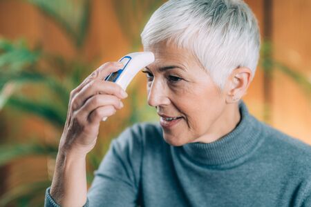 Senior Woman Measuring Body Temperature with Contactless Digital Thermometer at Home